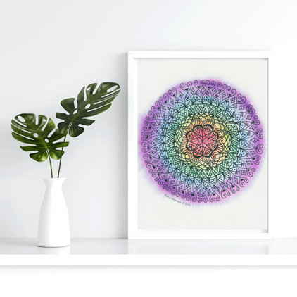 Mandala by Rachel Mambach Art in a white picture frame next to a white vase with two monsterra leaves